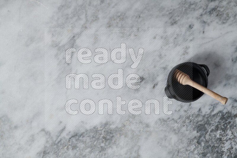 وعاء فخاري أسود مع ملعقة عسل خشبية بداخله على خلفية من الرخام الرمادي