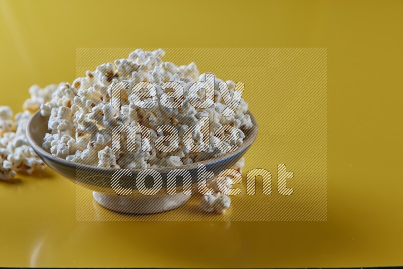 A multicolored ceramic plate full of popcorn with popcorn beside it on a yellow background in different angles