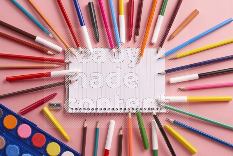A blank open notebook with coloring pens on rose background