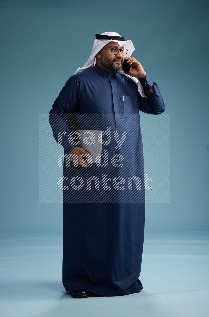Saudi Man with shimag Standing talking on phone on blue background