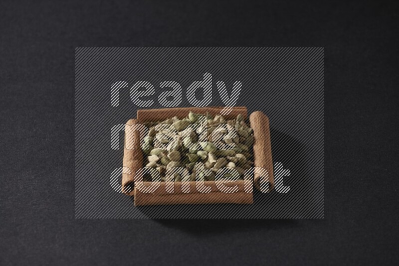 أربعة من أعواد القرفة مكونة شكل مربع بداخلها حبوب الهيل علي خلفية سوداء