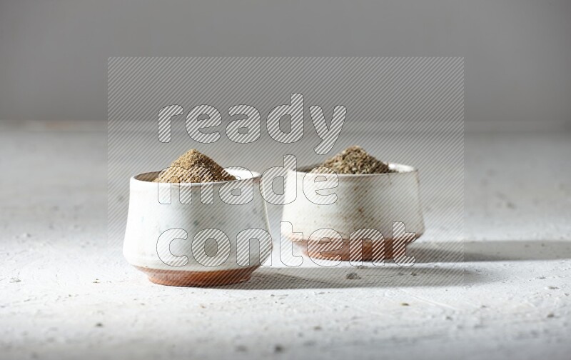 2 beige bowls full of cumin seeds and powder on a textured white flooring