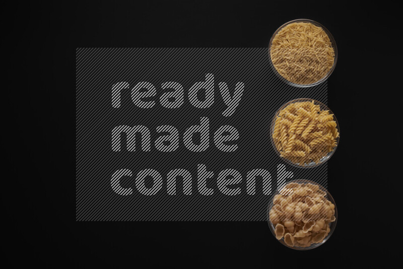 Different pasta types in 3 glass bowls on black background