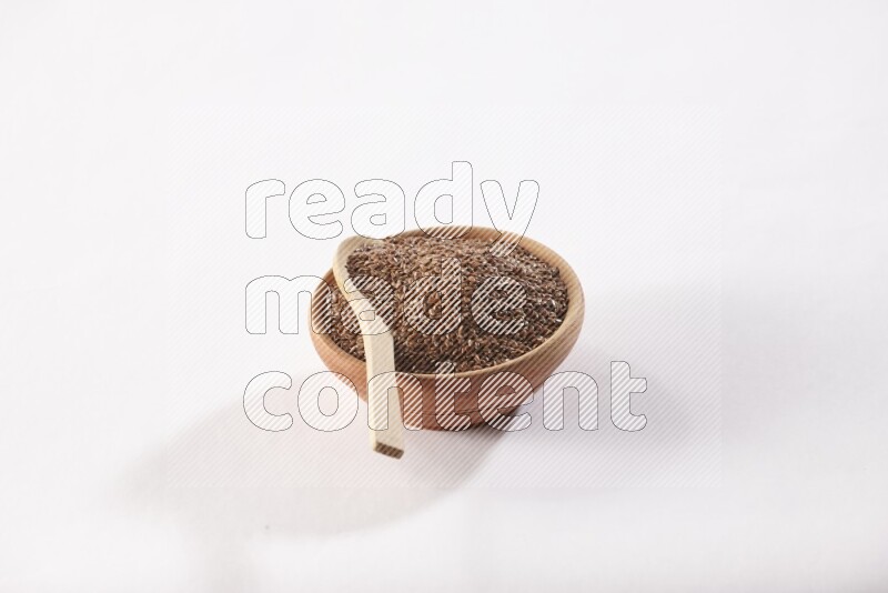 A wooden bowl full of flax seeds and a wooden spoon full of flax seeds in it on a white flooring