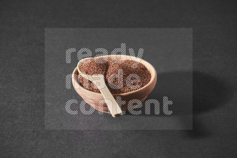 A wooden bowl full of garden cress seeds and a wooden spoon full of the seeds on it on a black flooring