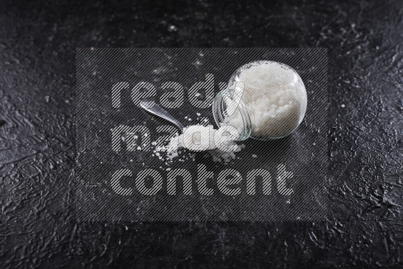 A glass jar full of coarse sea salt crystals on black background