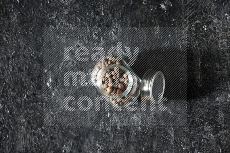 A glass spice jar full of allspice whole balls on a textured black flooring