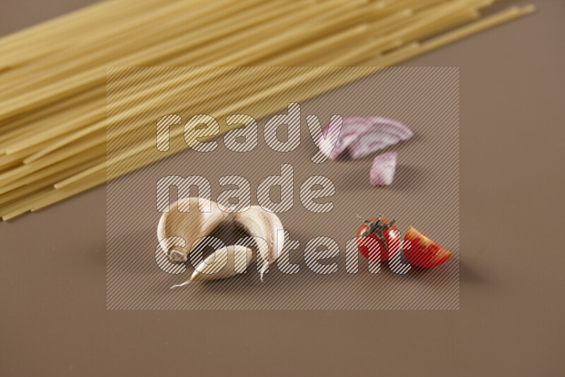 Raw pasta with different ingredients such as cherry tomatoes, garlic, onions, red chilis, black pepper, white pepper, bay laurel leaves, rosemary and cardamom on beige background