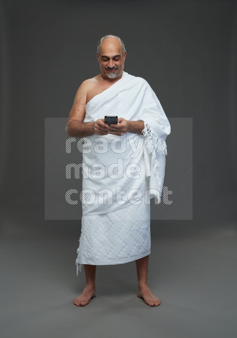 A man wearing Ehram Standing texting on phone on gray background