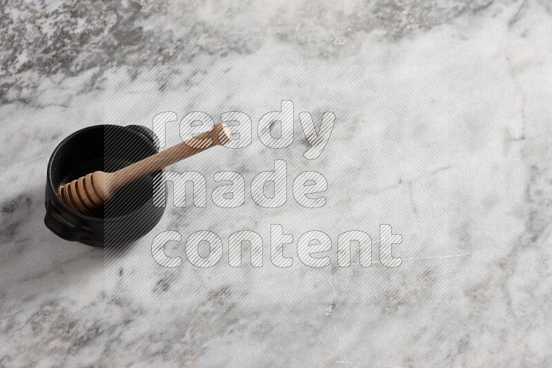 Black pottery bowl with wooden honey dipper in it on grey marble background