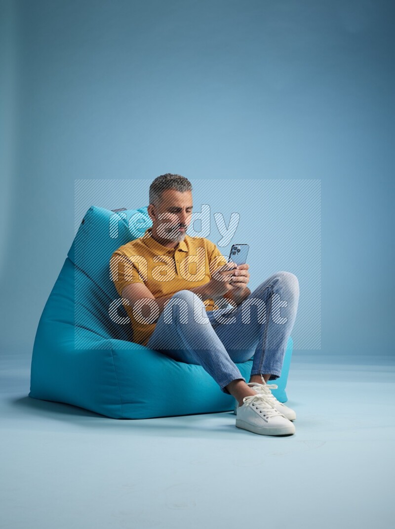 A man sitting on a blue beanbag and texting on phone