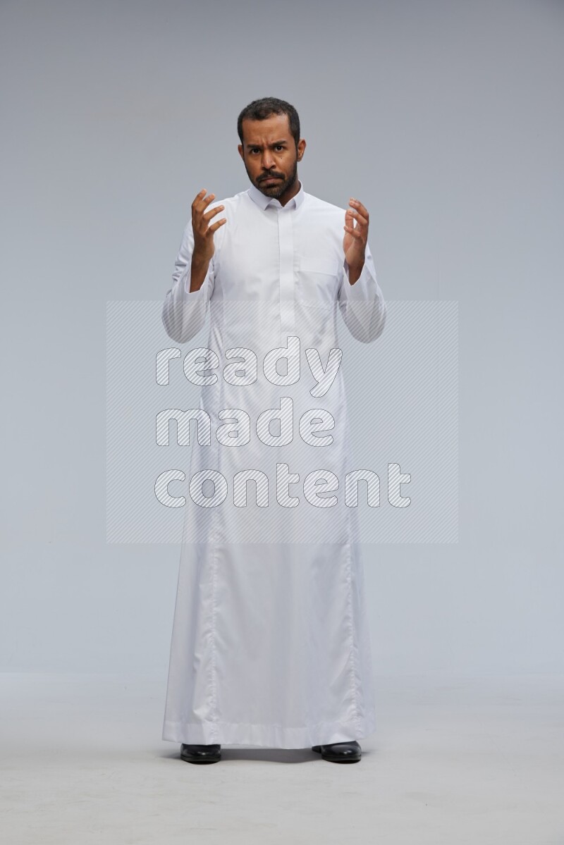 Saudi man Wearing Thob standing interacting with the camera on Gray background