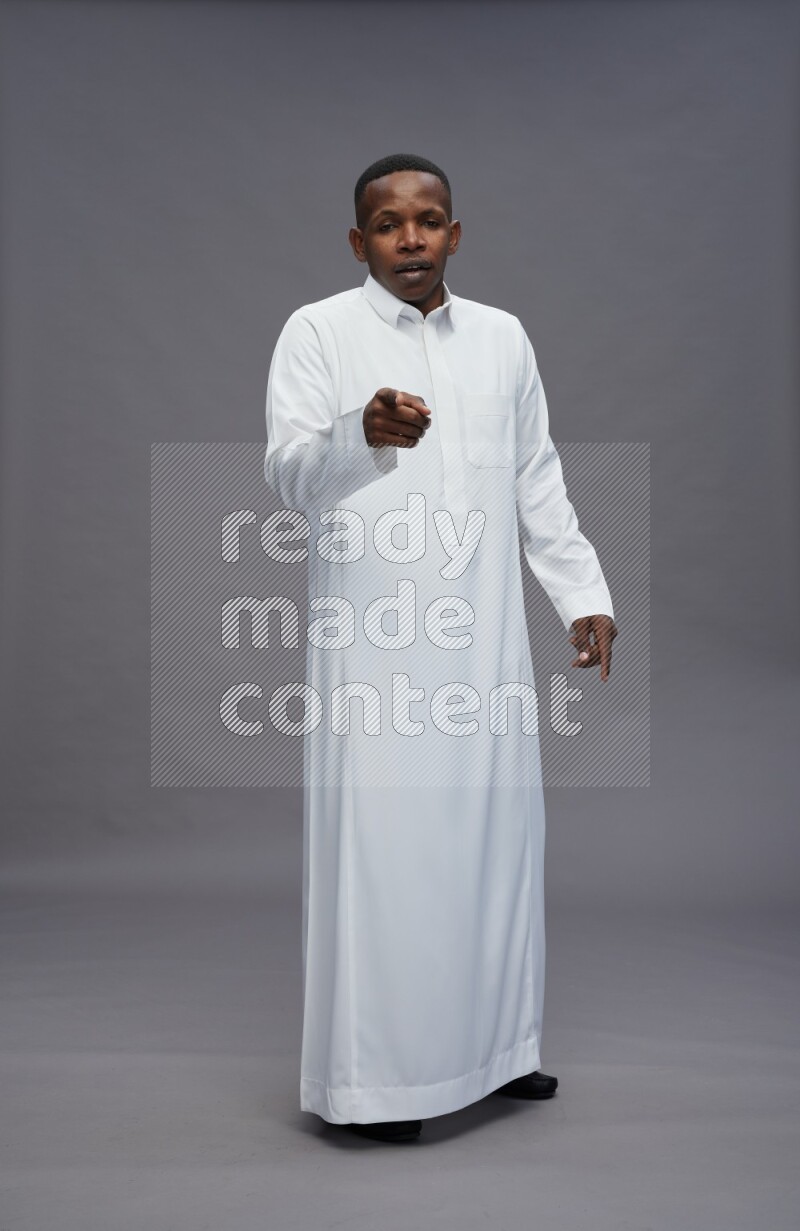 Saudi man wearing thob standing interacting with the camera on gray background