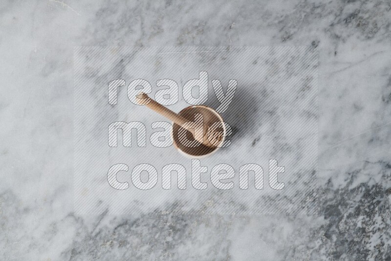 Multicolored pottery bowl with wooden honey dipper in it on grey marble background