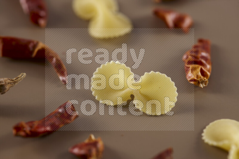 Raw pasta with different ingredients such as cherry tomatoes, garlic, onions, red chilis, black pepper, white pepper, bay laurel leaves, rosemary and cardamom on beige background