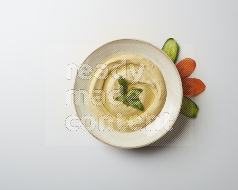 Hummus in a pottry plate garnished with mint  on a white background