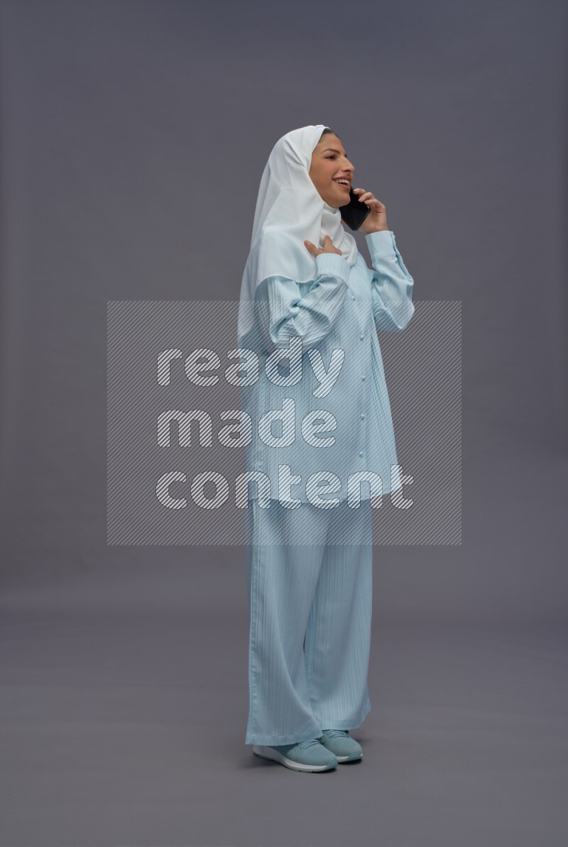 Saudi woman wearing hijab clothes standing talking on phone on gray background