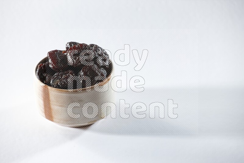 A beige ceramic bowl full of dried plums on a white background in different angles