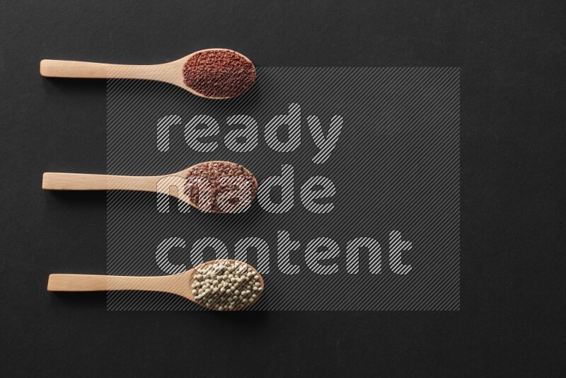 الفلفل الأسود وحبوب الخردل وحبة البركة وحب الرشاد والكمون و حبوب الكتان في معالق خشبية علي خلفية سوداء