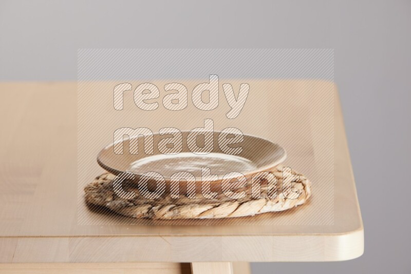 multi-colored pottery Plate placed on a small light colored straw placemat on the edge of wooden table