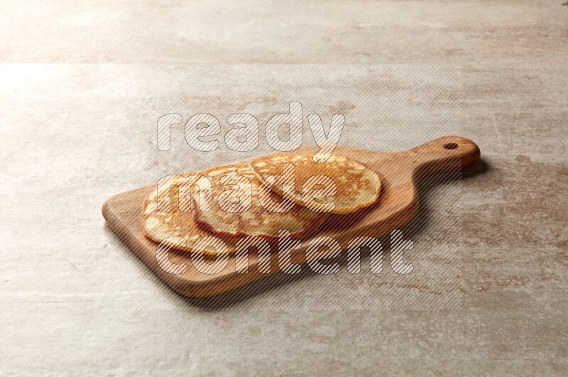 Three stacked plain pancakes on a wooden board on beige background