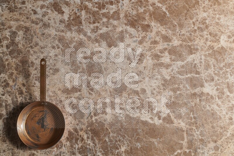 A small copper pan on beige marble background