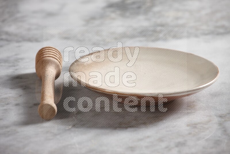 Beige pottery plate with wooden honey dipper on the side on grey marble background