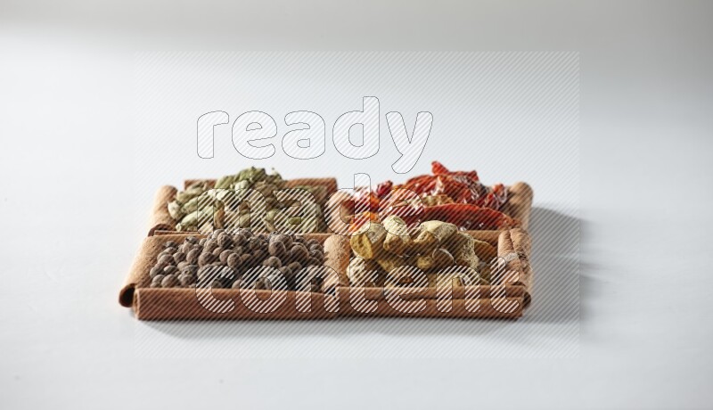 4 squares of cinnamon sticks full of dried red chilis, cardamom, turmeric fingers and allspice on white flooring