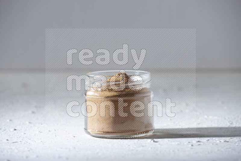 A glass jar full of allspice powder on a textured white flooring