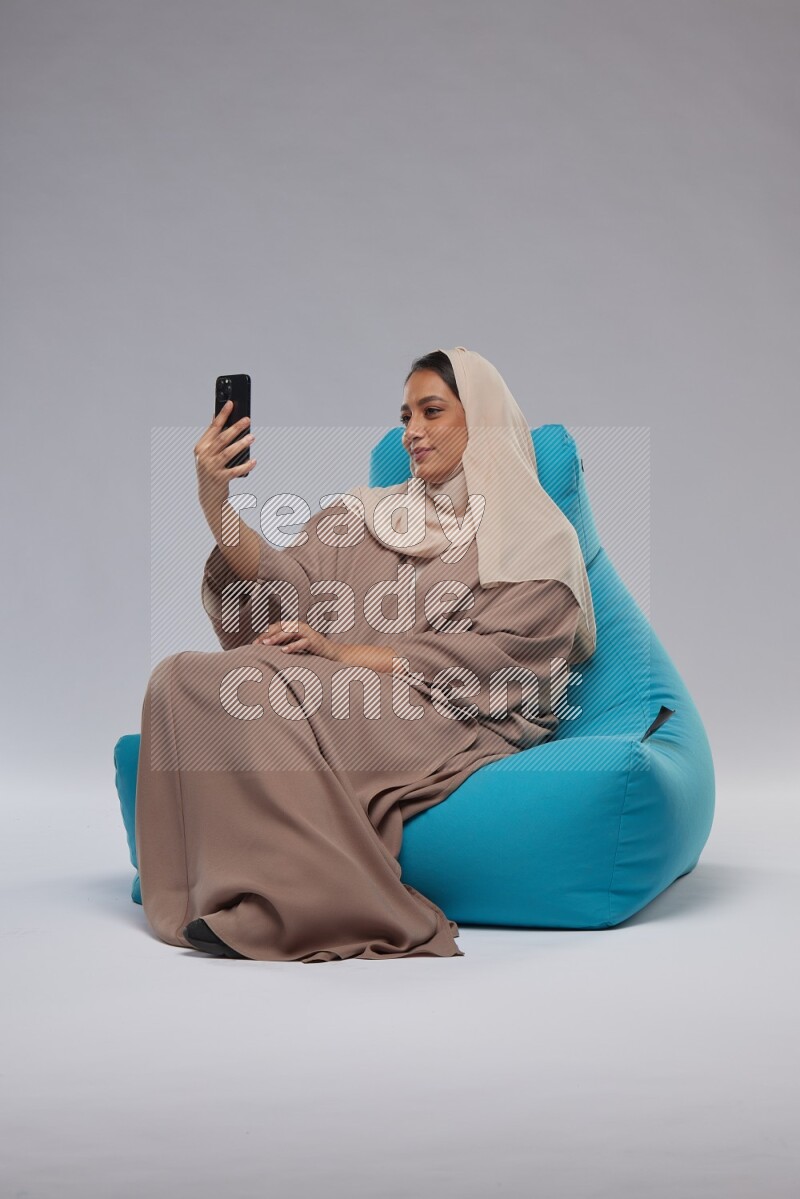 A Saudi woman sitting on a blue beanbag and taking selfie