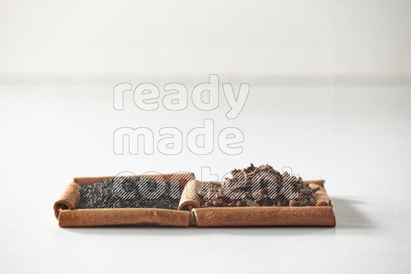 رمربعان من أعواد القرفة ممتلئان بالقرنفل وحبة البركة السوداء علي خلفية بيضاء