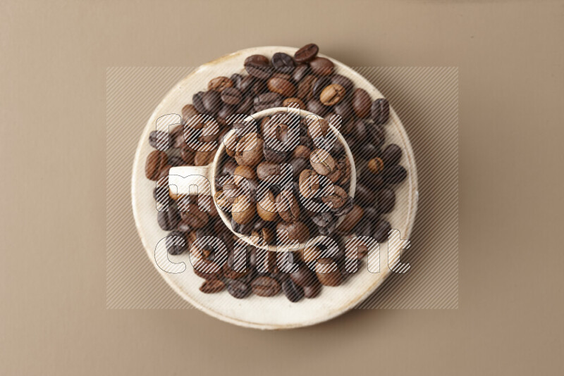 A beige pottery cup full of roasted coffee beans on beige background