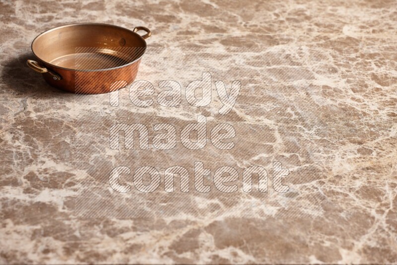 A small copper pan on beige marble background