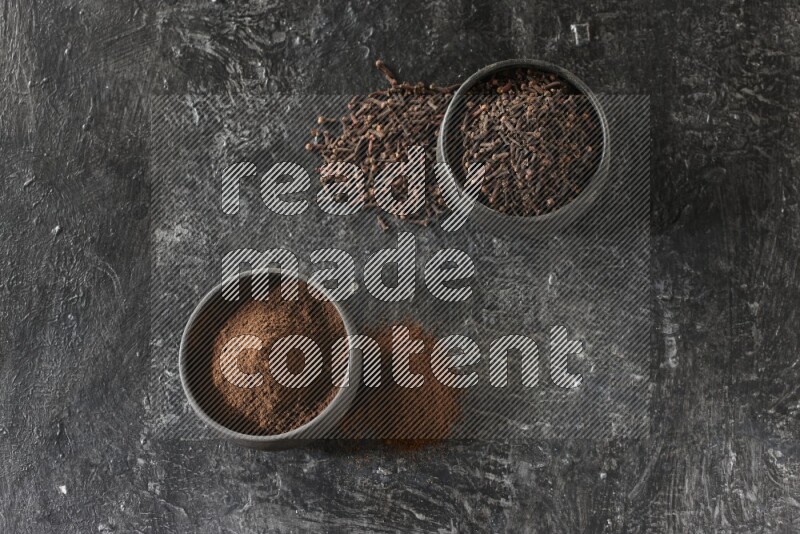 وعاءين من الفخار الأسود أحدهما ممتلئي بحبوب القرنفل والآخر ممتلئ ببودرة القرنفل على خلفية سوداء