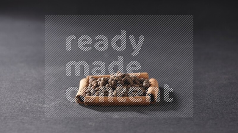 أربعة من أعواد القرفة مكونة شكل مربع بداخلها بهار الفلفل الحلو علي خلفية سوداء