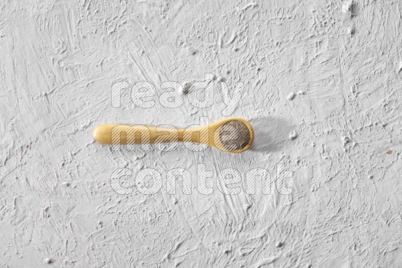 A wooden spoon full of black pepper powder on a textured white flooring