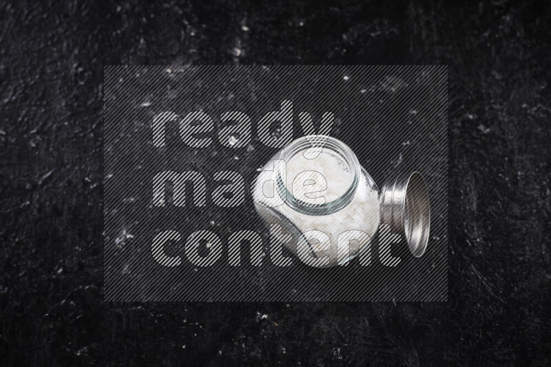 A glass jar full of coarse sea salt crystals on black background