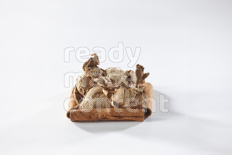 أربعة من أعواد القرفة مكونة شكل مربع بداخلها زنجبيل مجفف علي خلفية بيضاء