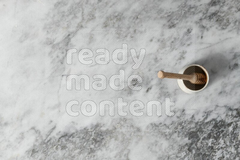 Beige pottery bowl with wooden honey dipper in it on grey marble background