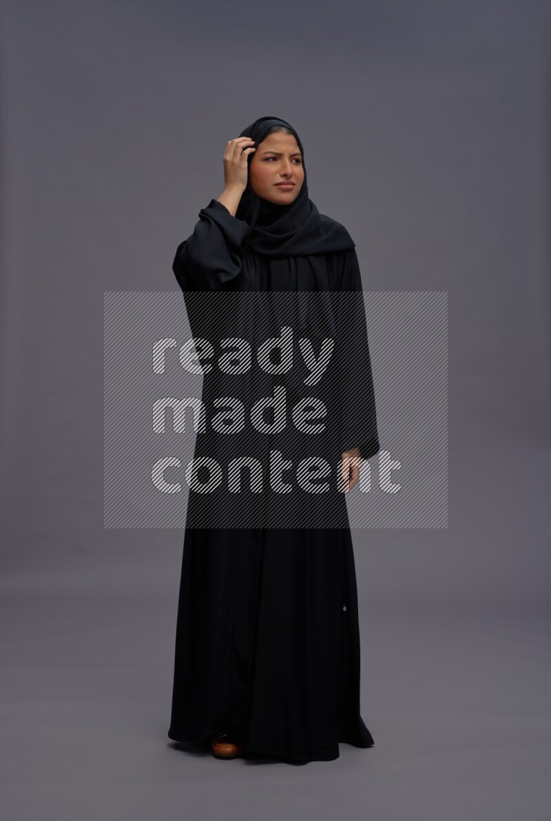 Saudi woman wearing Abaya standing interacting with the camera on gray background