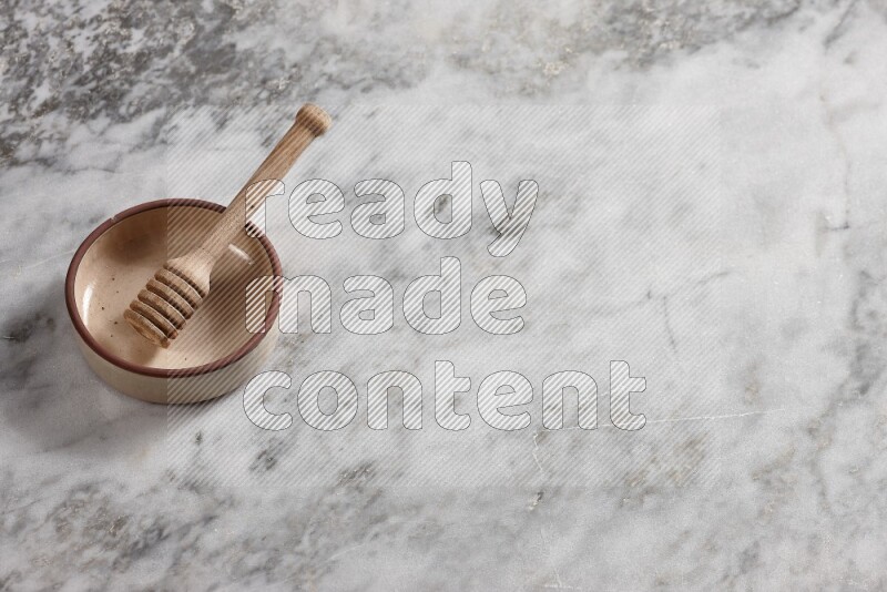 Beige Pottery oven bowl with wooden honey handle on the side with grey marble flooring, 65 degree angle