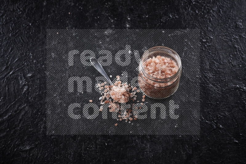 A glass jar full of coarse himalayan salt crystals on black background