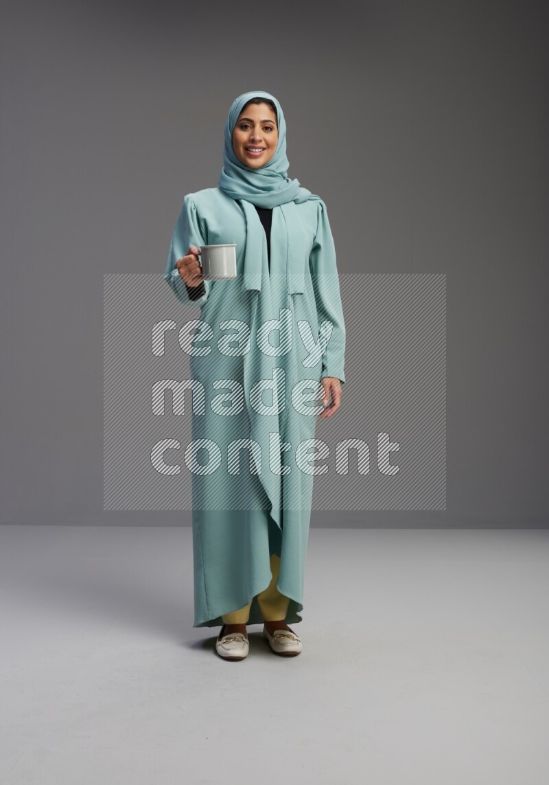 Saudi Woman wearing Abaya standing  holding a mug on Gray background