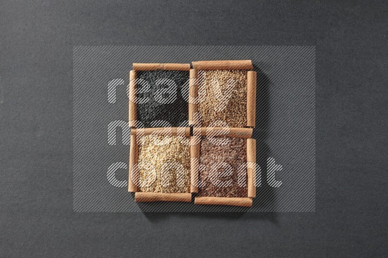 4 squares of cinnamon sticks full of black seeds, sesame, flaxseeds and mustard seeds on black flooring