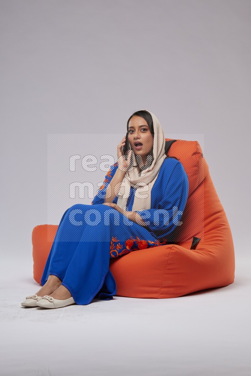 A Saudi woman wearing Jalabiya sitting on an orange beanbag and talking on the phone