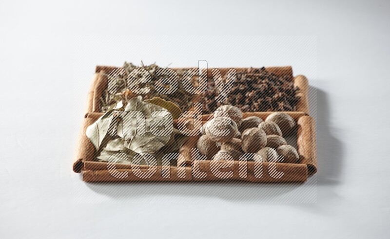 4 مربعات من أعواد القرفة ممتلئة بأوراق الغار والريحان المجفف والقرنفل وجوزة الطيب على أرضية بيضاء