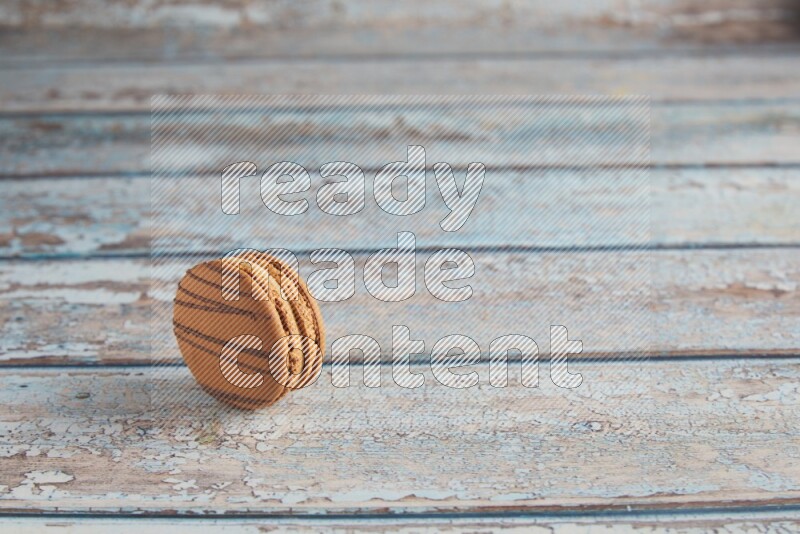 45º Shot of light brown Almond Cream macaron on light blue wooden background