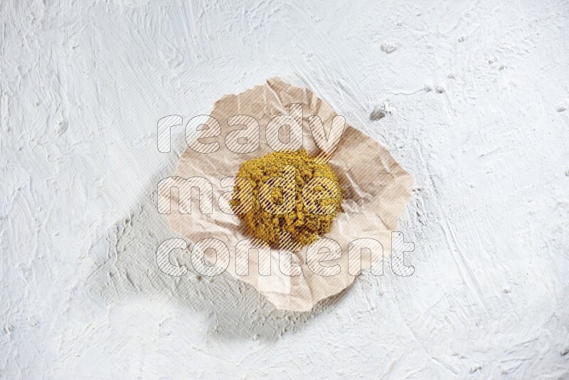Turmeric powder in a crumpled piece of paper on textured white flooring