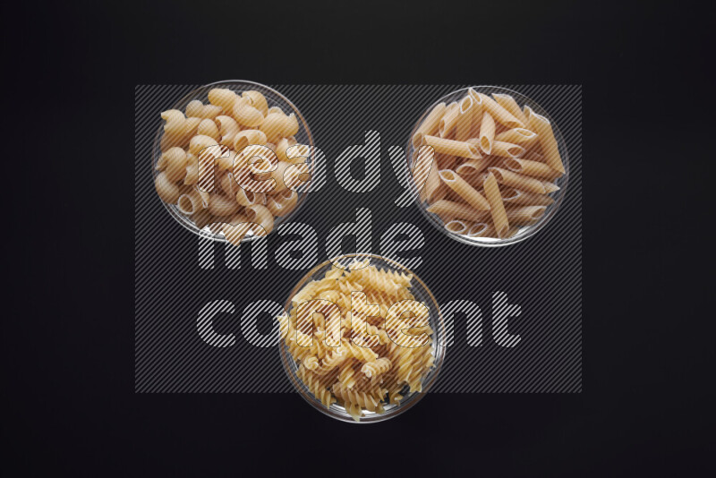 Different pasta types in glass bowls on black background