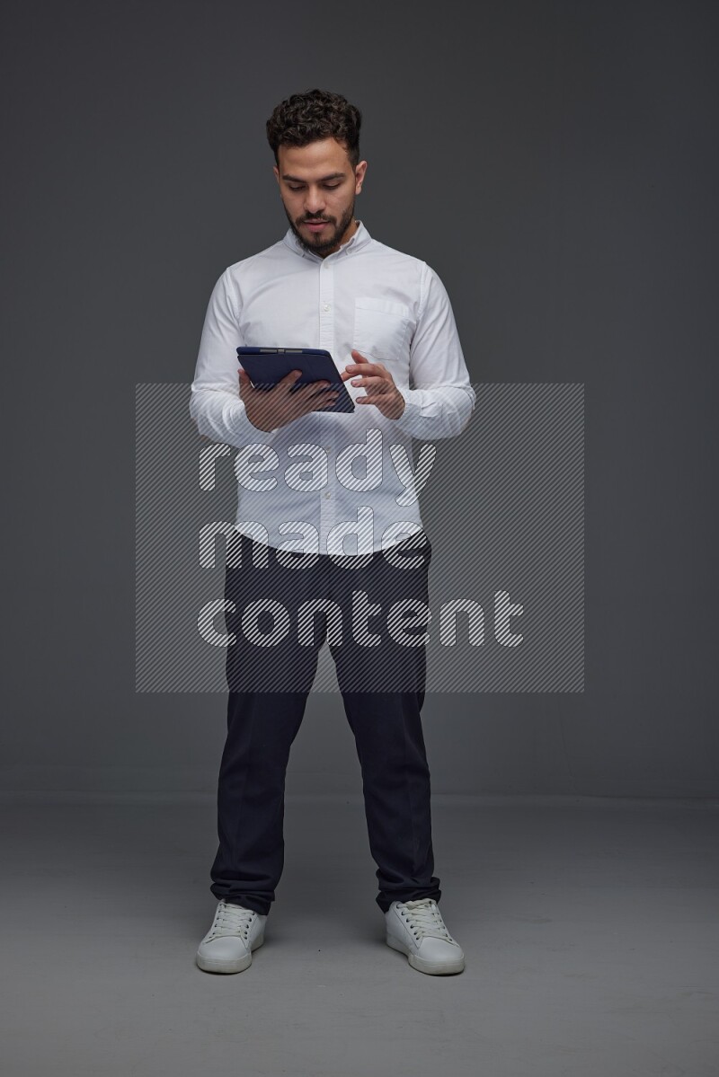 A man wearing smart casual standing and using his tablet eye level on a gray background